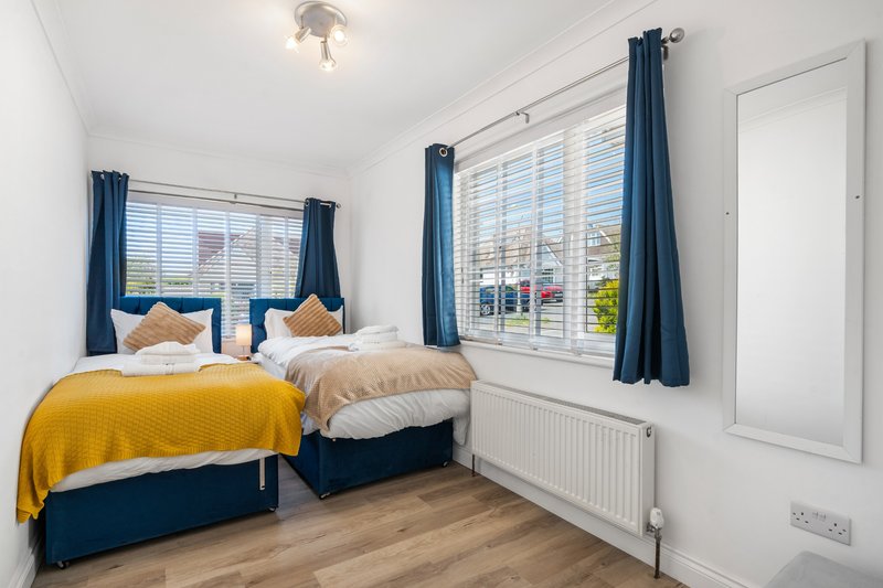 Bright bedroom with two single beds, yellow and blue bedding, large windows with blue curtains, wooden floor