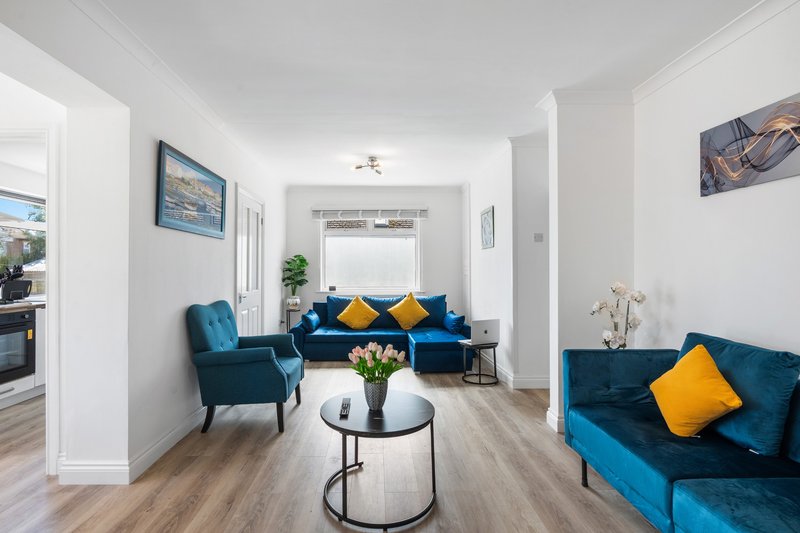 Modern open-plan living area with blue upholstered seating, yellow accent cushions, and round white table