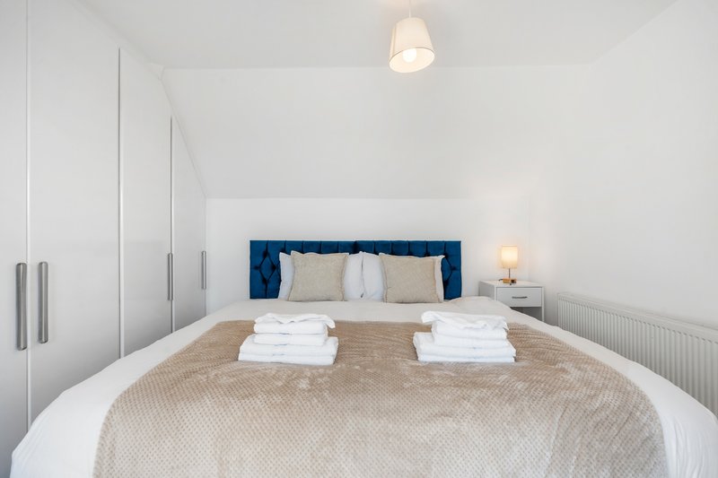 Modern bedroom with double bed, blue headboard, white walls, and pendant lighting