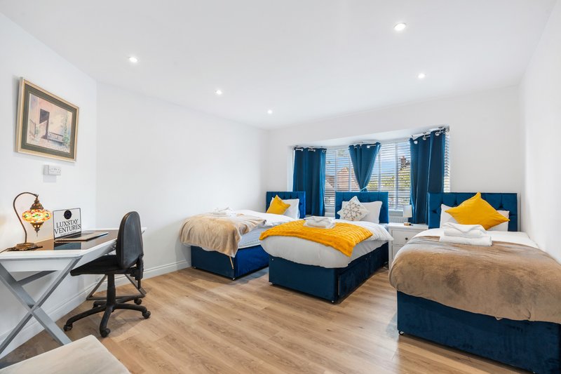 Bright bedroom with two single beds, blue headboards, yellow pillows, desk with chair and window with blue curtains