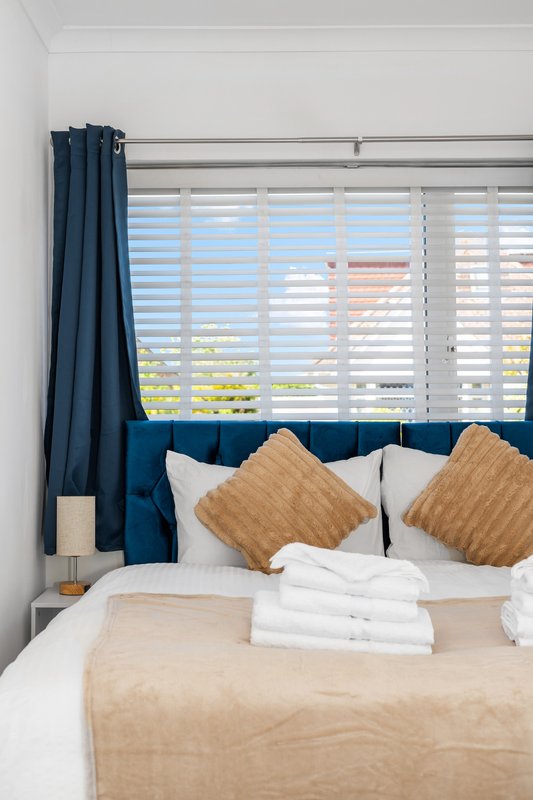 Bedroom with blue upholstered headboard, white pillows, mustard cushions, and shuttered windows with sea view
