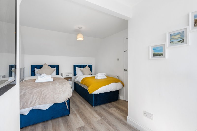 Bright bedroom with two single beds, blue headboards, wooden floor and framed artwork