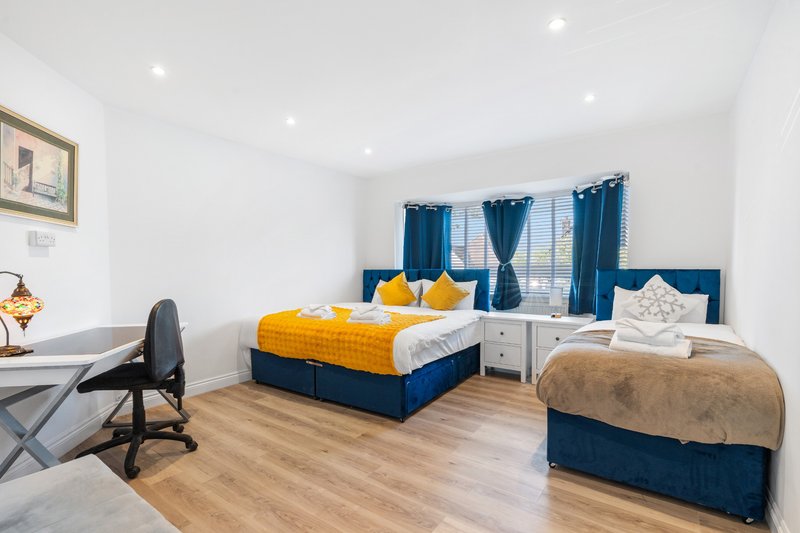 Bright bedroom with double bed, yellow bedding, blue headboard, wooden floor and desk