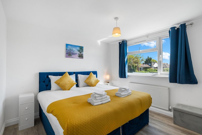 Bright bedroom with blue upholstered bed, yellow bedding, pendant light and garden views