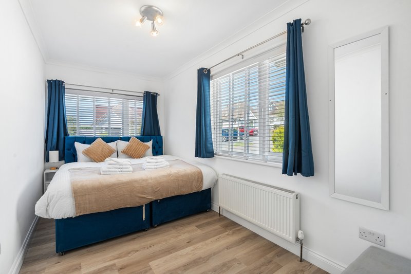 Bright bedroom with double bed, blue headboard and curtains, wooden floor