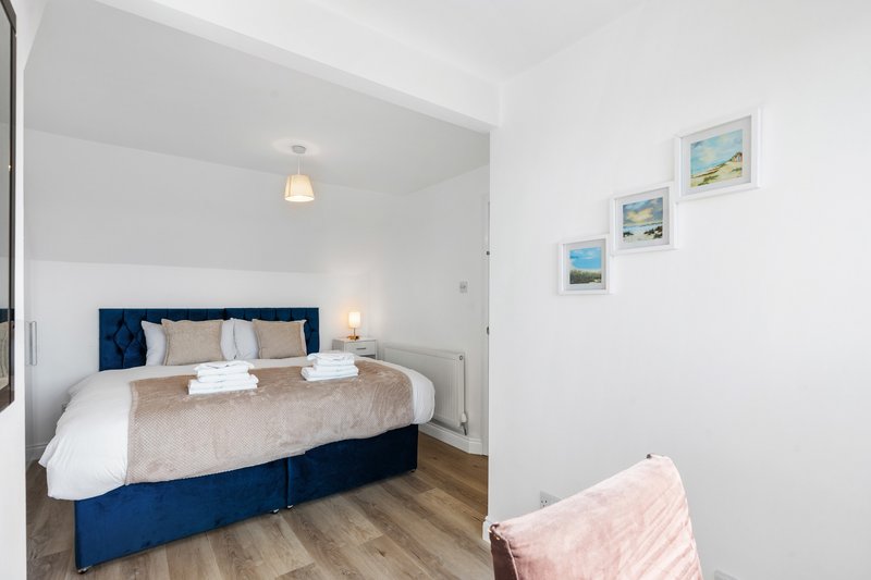 Modern bedroom with double bed, navy headboard, wooden floor, and framed coastal artwork