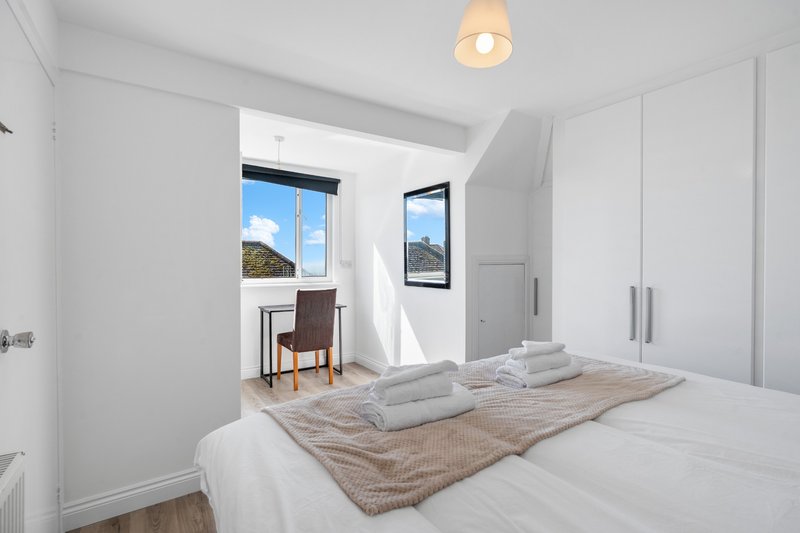 Bright modern bedroom with double bed, white wardrobes, wooden floor and windows with views