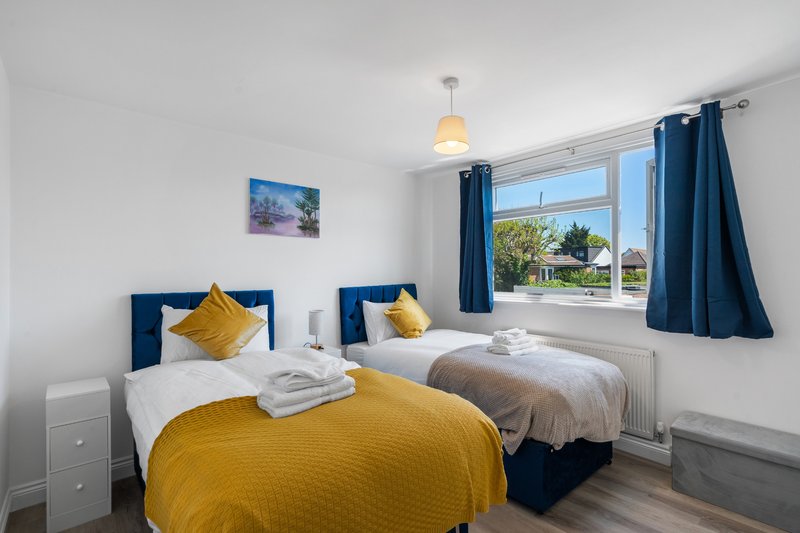 Bright bedroom with two single beds, blue headboards, yellow cushions and throws, large window with garden view