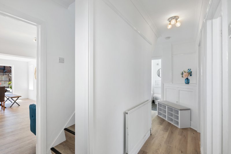 Bright white hallway with wooden flooring, staircase, and storage shelving unit