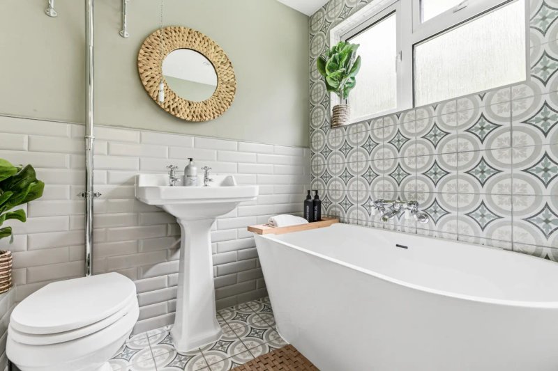 Modern bathroom with freestanding bathtub, pedestal sink, toilet, and decorative tile accents