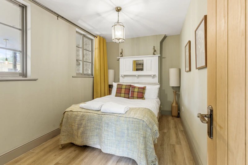 Compact bedroom with single bed, wooden flooring, yellow curtains and pendant light fixture