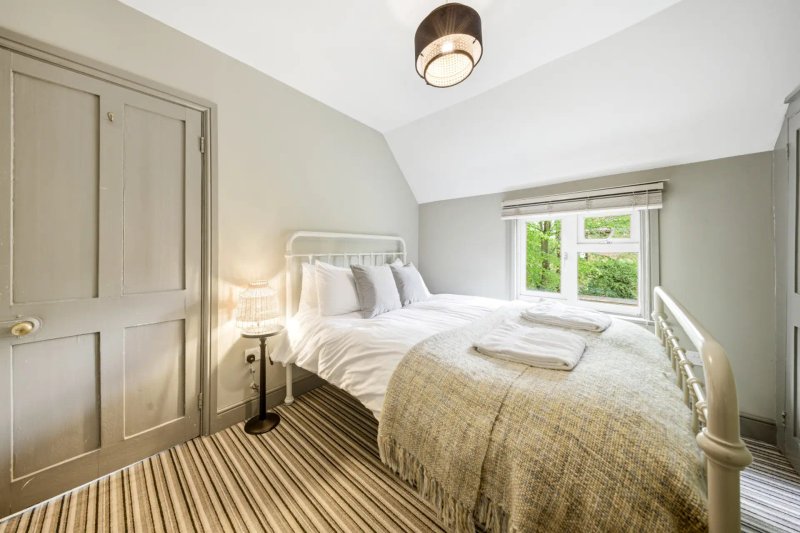Bright bedroom with white metal bed frame, striped carpet, wooden wardrobe and natural light from window