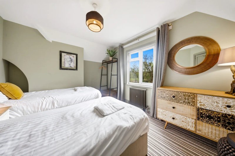 Bright bedroom with two single beds, wooden dresser, round mirror and garden view
