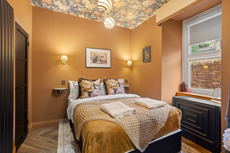 Warm bedroom with double bed, gold bedding, framed artwork, and window with brick view