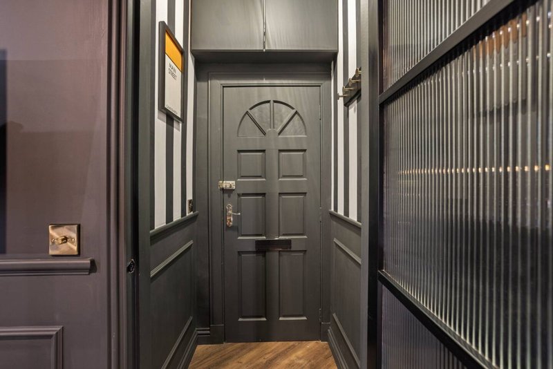 Narrow hallway with black front door, wooden floor, and decorative side panels