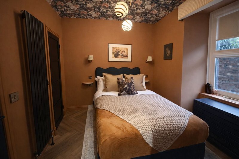 Warm bedroom with double bed, black headboard, ochre walls, pendant light and framed artwork