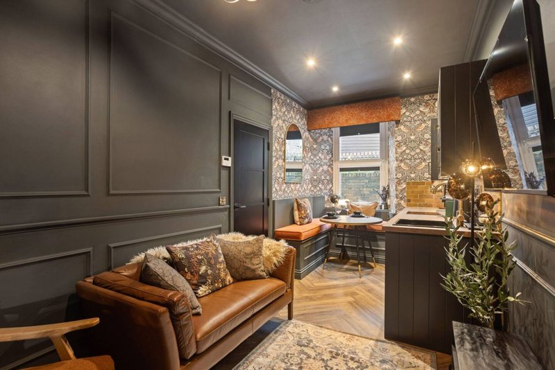 Modern living room with tan leather sofa, patterned cushions, dark wall panelling and desk area by window