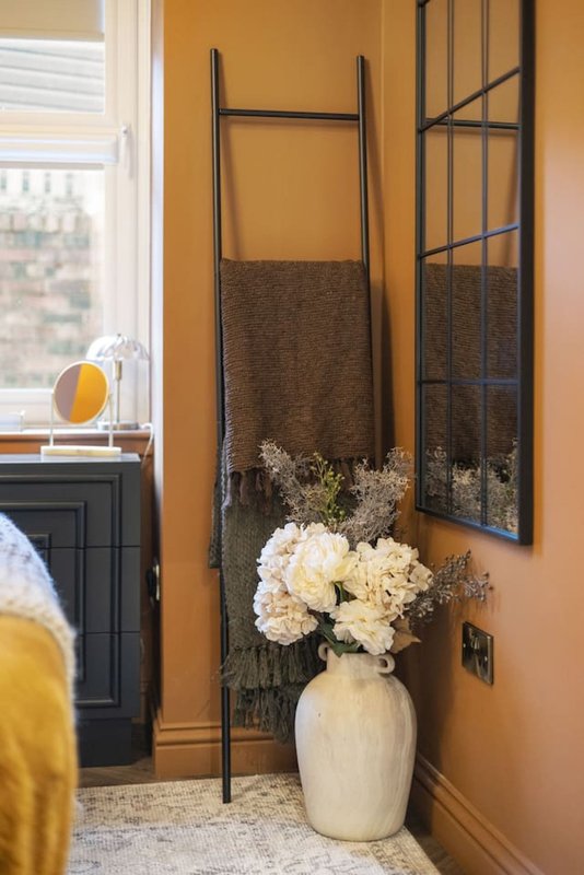 Orange bedroom corner with white flowers in vase, towel ladder and window