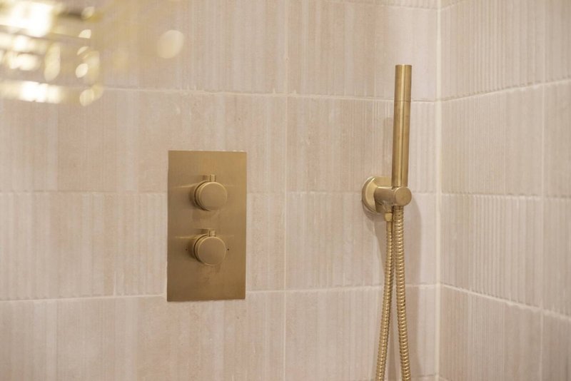 Bathroom shower wall with brass valve controls and handheld showerhead
