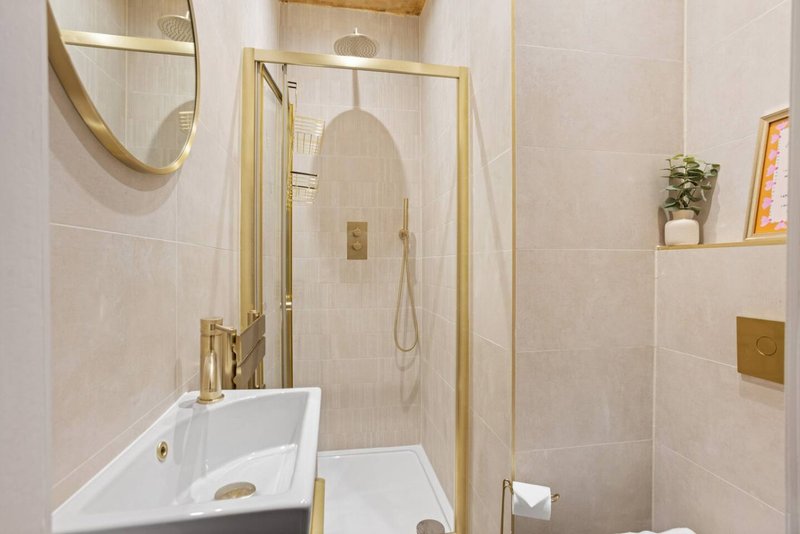 Modern bathroom with white sink, gold fixtures, shower enclosure and neutral tiles