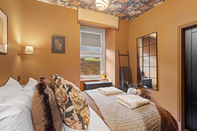 Warm orange bedroom with two beds, patterned throws, window view, and decorative mirror
