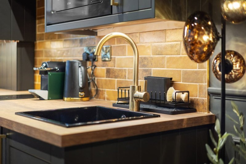 Modern kitchen with black sink, brass tap, tiled backsplash and decorative bowls