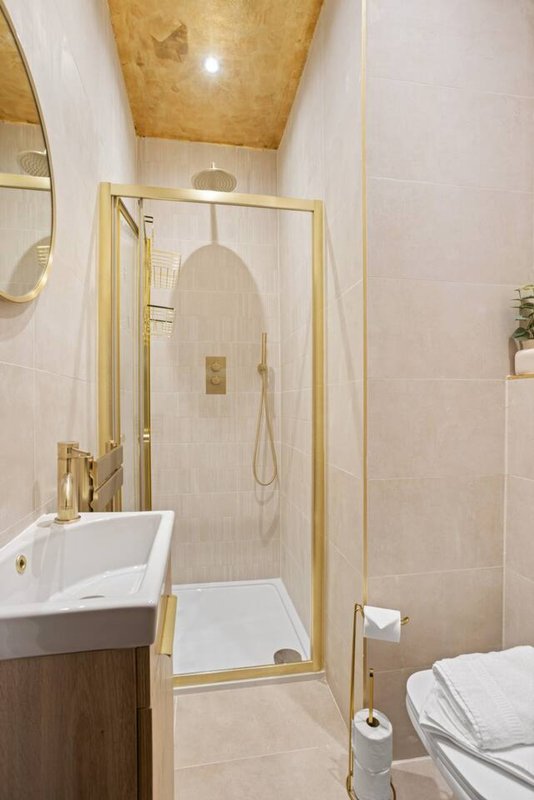 Modern bathroom with walk-in shower, white sink vanity, toilet and gold fixtures