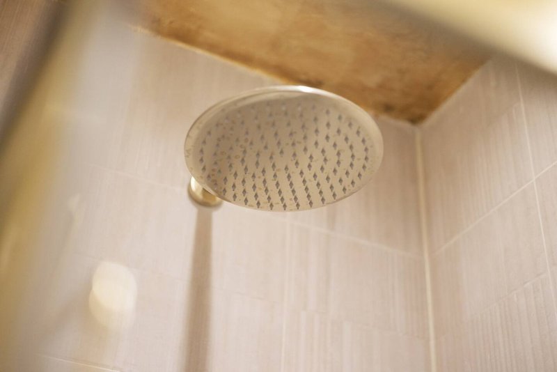 Overhead shower head mounted on white tiled bathroom ceiling
