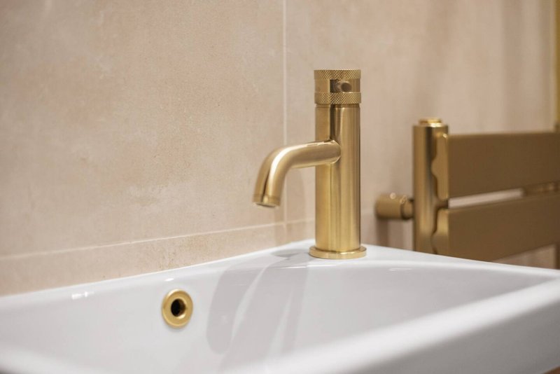 Modern bathroom sink with brass faucet and beige tile wall