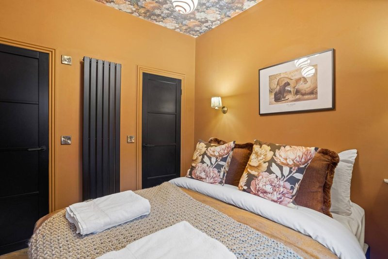 Bedroom with double bed, decorative pillows, gold walls, black doors and framed artwork
