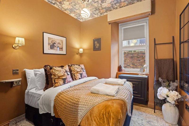 Warm yellow bedroom with double bed, wall sconces, framed artwork, and window with brick view