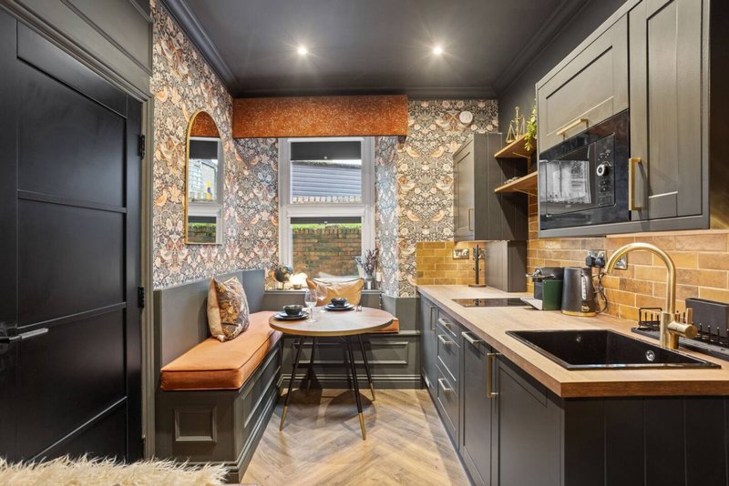 Modern kitchen and dining area with patterned wallpaper, built-in bench seating, round table and gray cabinetry