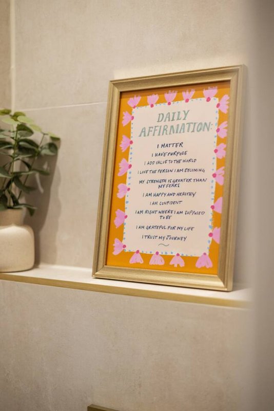 Framed motivational poster with daily affirmations on shelf next to potted plant