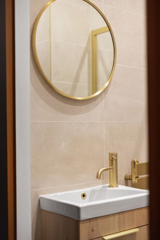 Bathroom vanity with white basin, gold faucet, and circular brass mirror
