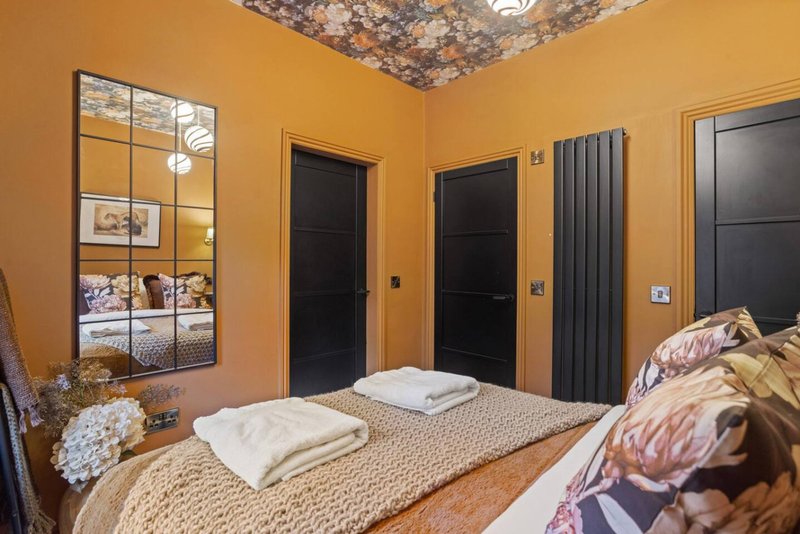 Bedroom with orange walls, double bed, mirror, black doors and textured ceiling