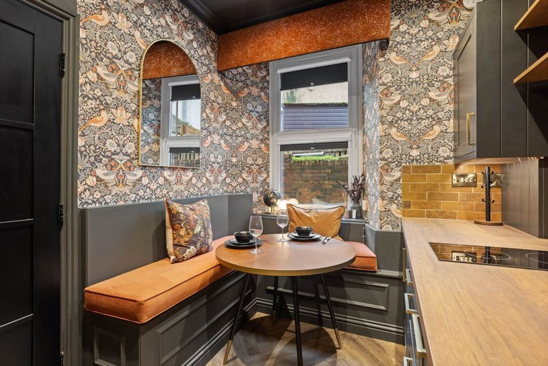 Compact kitchen nook with patterned wallpaper, built-in seating, round dining table and window