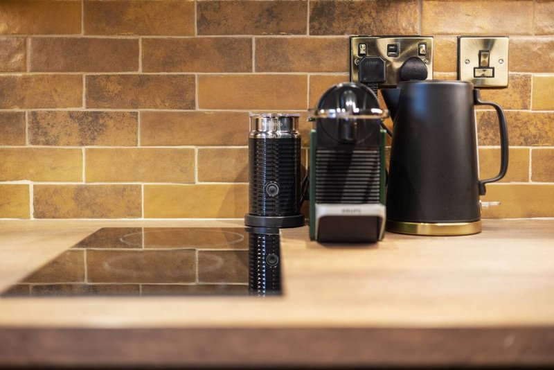 Kitchen countertop with coffee maker, kettle, and accessories against terracotta tile backsplash