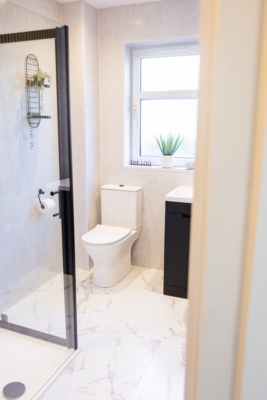 Modern bathroom with walk-in shower, toilet, window, and marble-effect flooring