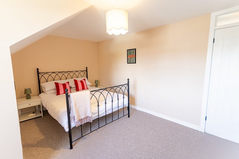 Bedroom with metal frame bed, red cushions, cream walls, ceiling light fixture