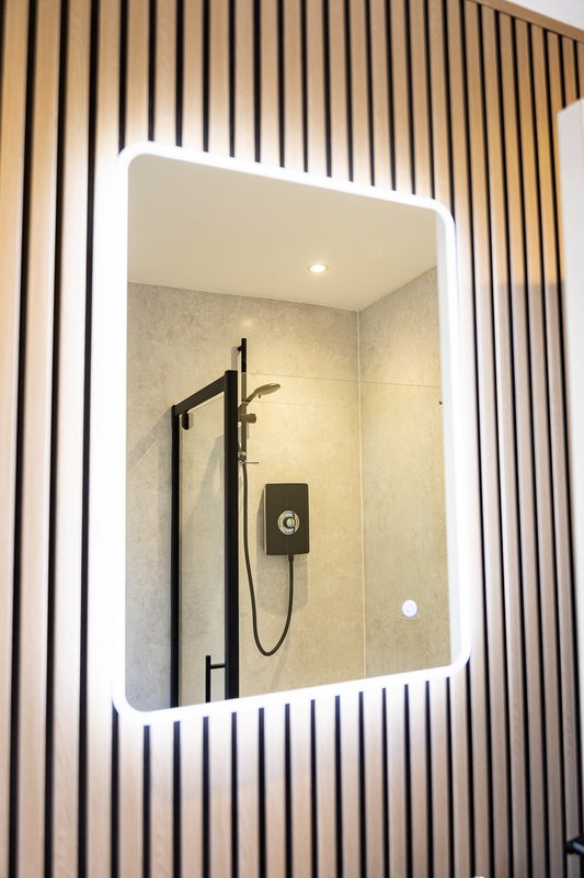Modern bathroom mirror with LED lighting and black shower fixture visible in reflection