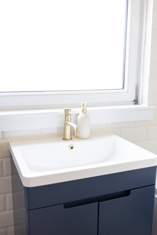 Modern bathroom sink with navy vanity, brass faucet, and window above