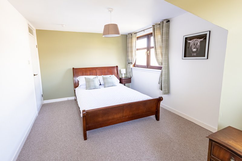 Bedroom with wooden double bed, white bedding, beige walls, carpet flooring and window.