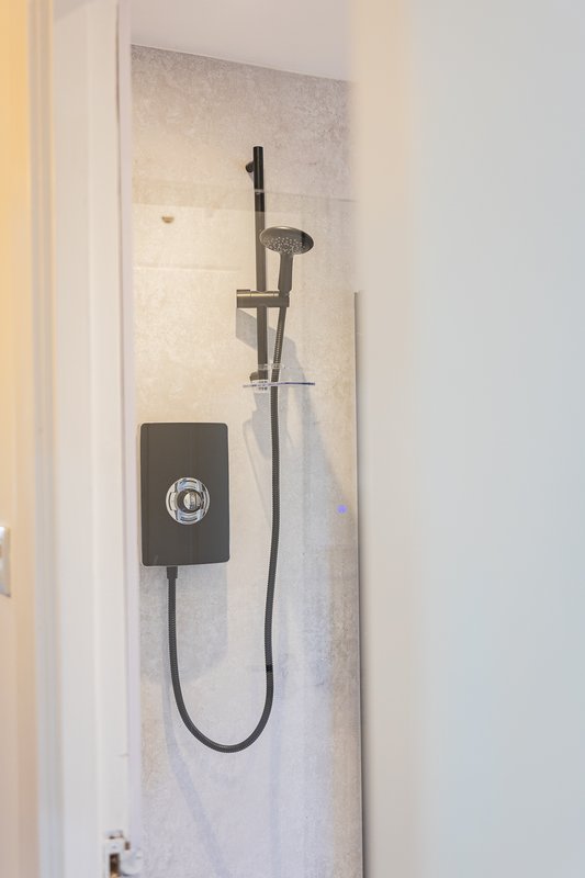 Compact shower enclosure with black electric shower unit and handheld showerhead
