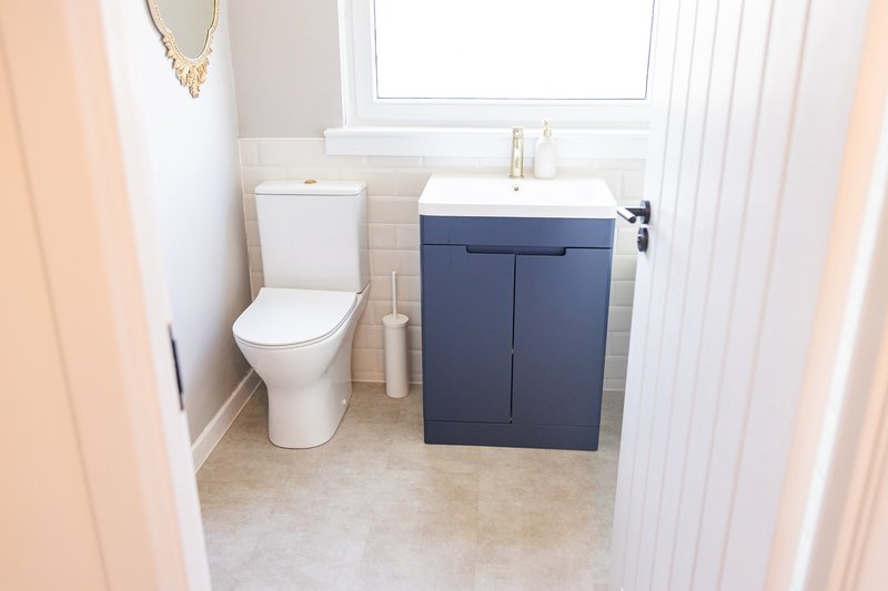 Modern bathroom with white toilet, navy vanity unit and sink, pale tile flooring