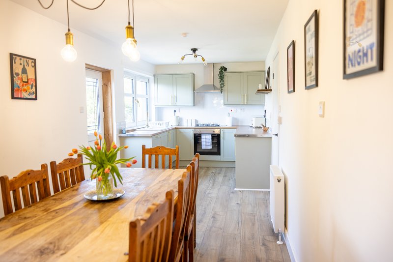 Open-plan kitchen and dining area with wooden table, chairs, pendant lights and modern appliances