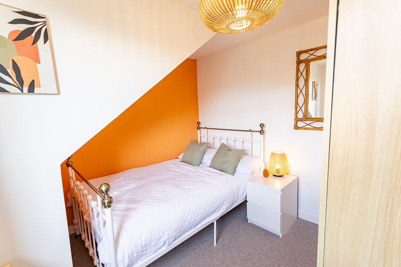 Bedroom with single bed, white bedding, orange accent wall, and bedside lamp