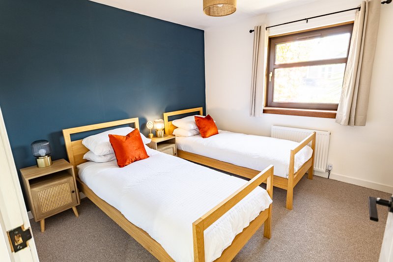 Bright bedroom with two single beds, wooden frames, white bedding, orange cushions, blue accent wall