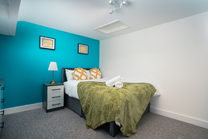 Bedroom with turquoise accent wall, double bed, olive bedding, and white bedside lamp