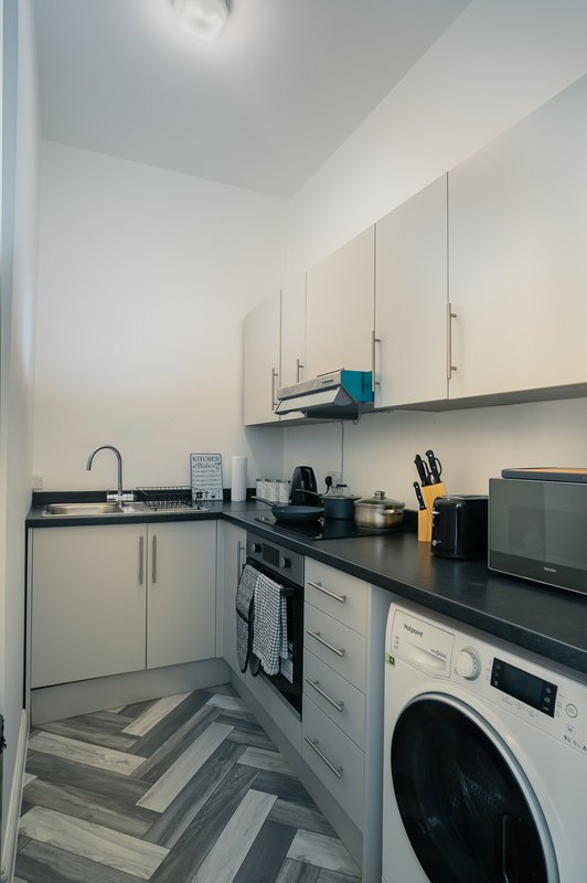 Modern kitchen with white cabinets, black countertop, integrated appliances and washing machine