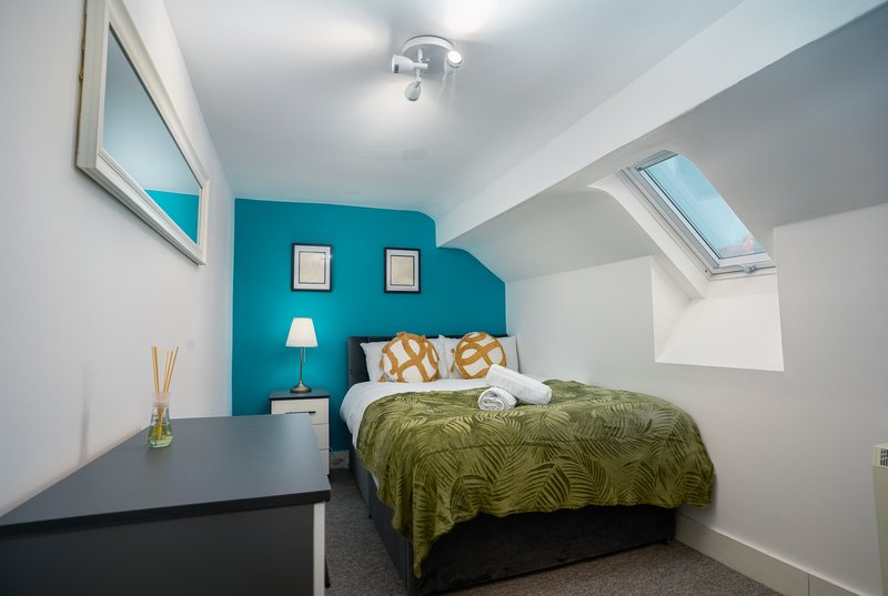 Bright bedroom with turquoise accent wall, double bed, desk, and skylights